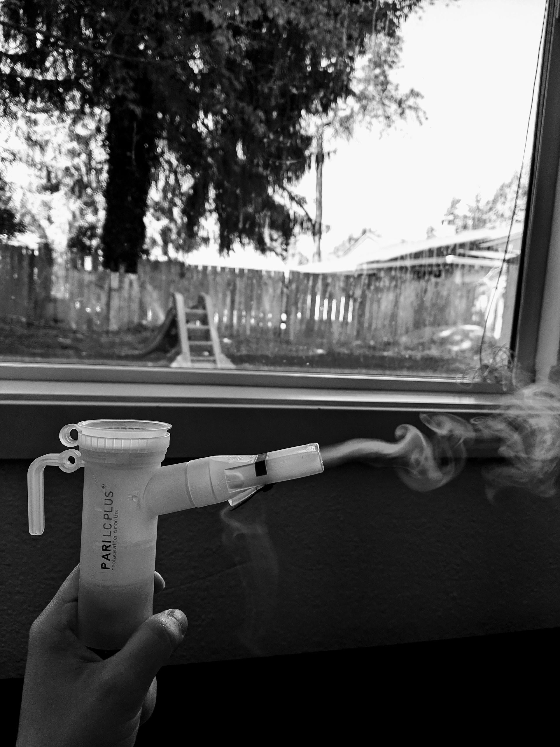 A hand holding a nebulizer releasing mist in front of a window