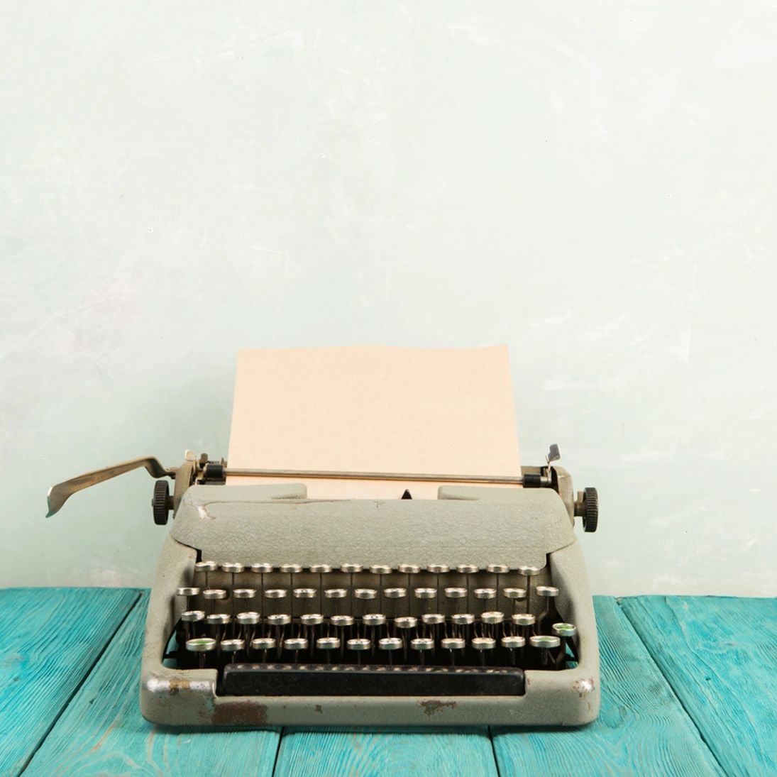 A vintage typewriter with a blank sheet of paper on a teal wooden table