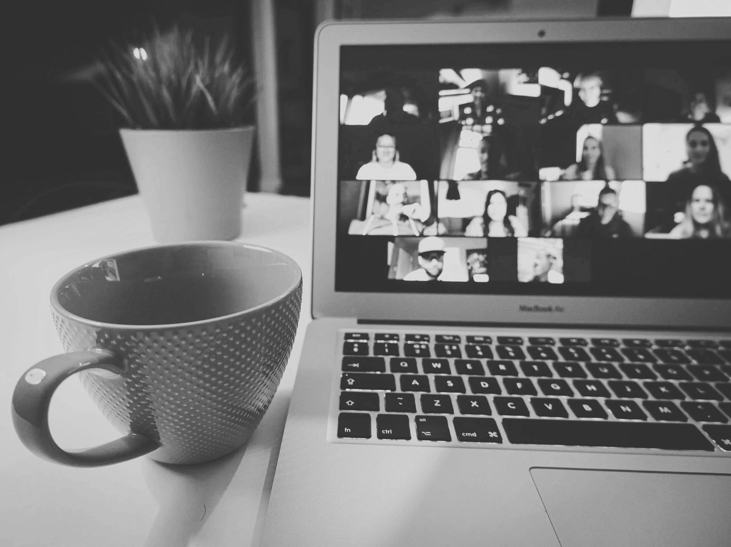 A laptop showing a video call with a grid of participants, next to a coffee mug